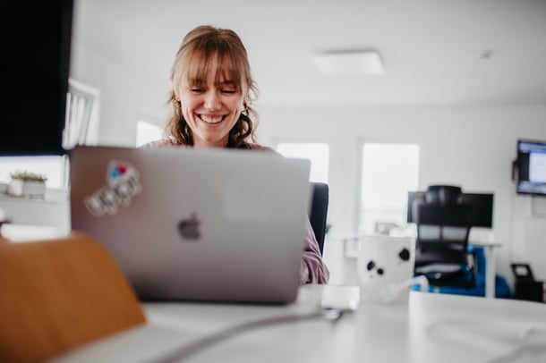 Eine junge Frau arbeitet im modernen Büro und lächelt, an ihrem Laptop ist das uppr-Logo