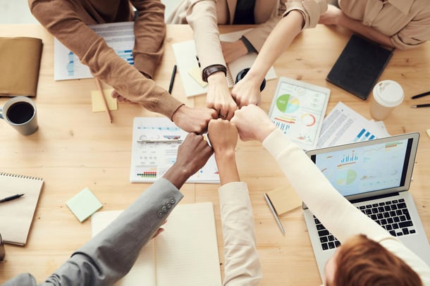 Teammitglieder feiern ihren gemeinsamen Erfolg und geben sich Fistbumps am Besprechungstisch